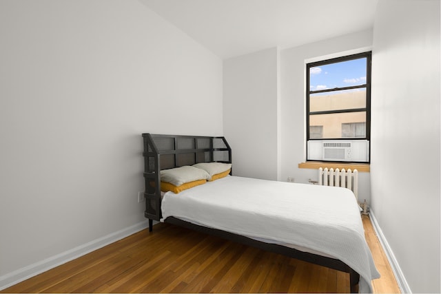 bedroom with cooling unit, baseboards, radiator, and wood finished floors