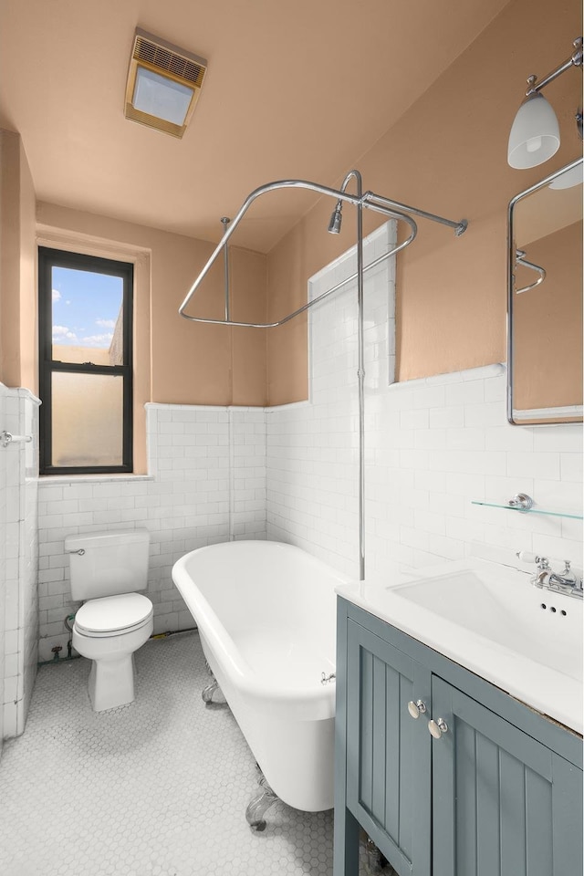 full bathroom with vanity, a wainscoted wall, visible vents, a soaking tub, and tile walls