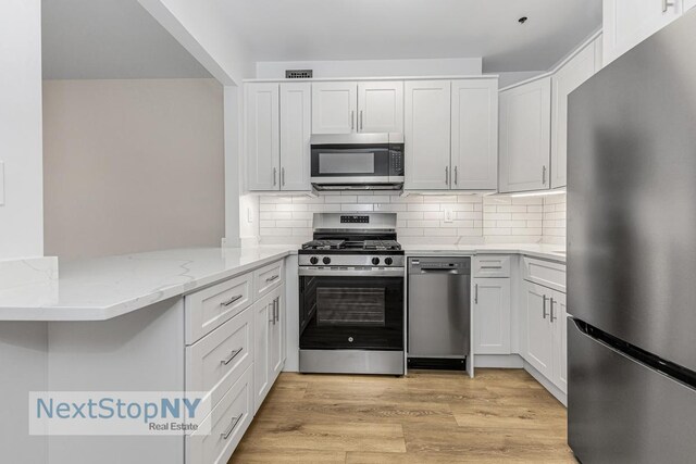 kitchen with light stone counters, tasteful backsplash, appliances with stainless steel finishes, light wood-style floors, and white cabinetry