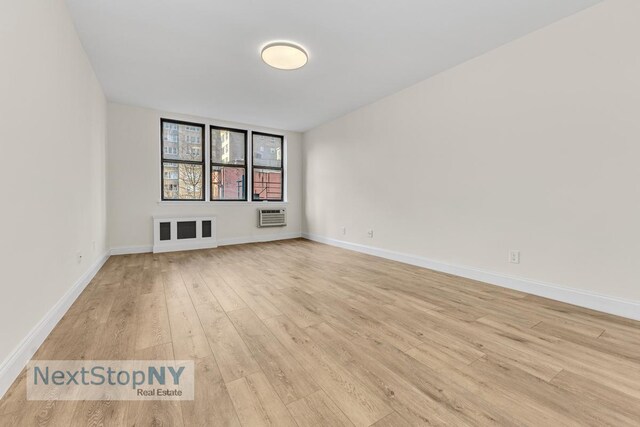 unfurnished room featuring light wood-style floors, baseboards, and a wall mounted air conditioner