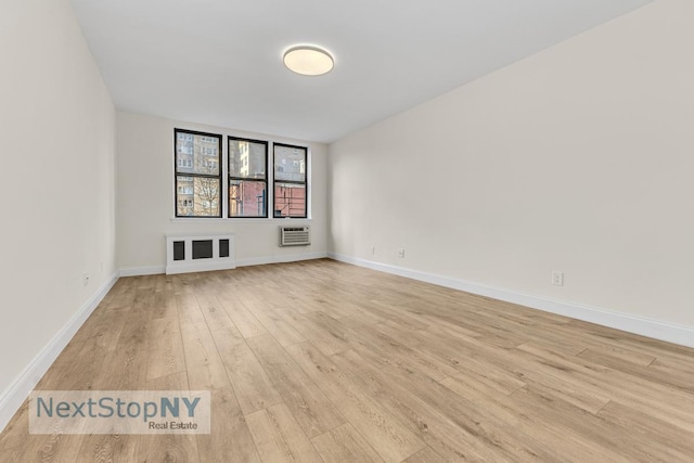 empty room featuring light wood-style flooring, baseboards, and a wall unit AC