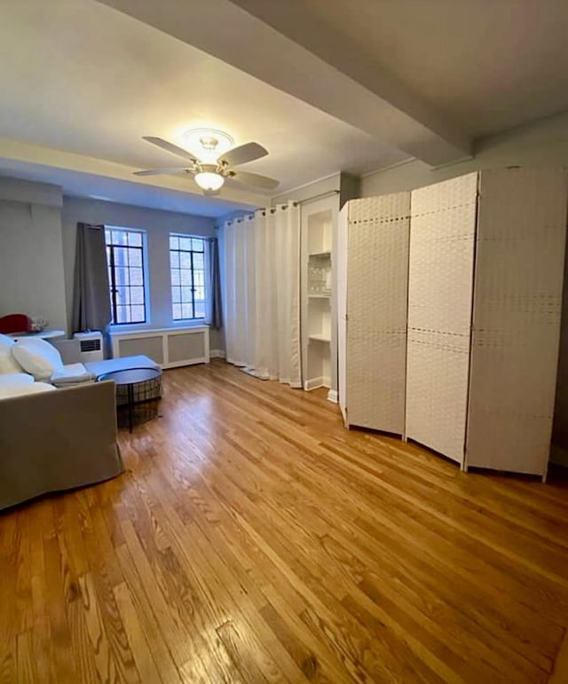 unfurnished bedroom featuring radiator, a ceiling fan, wood finished floors, and beamed ceiling