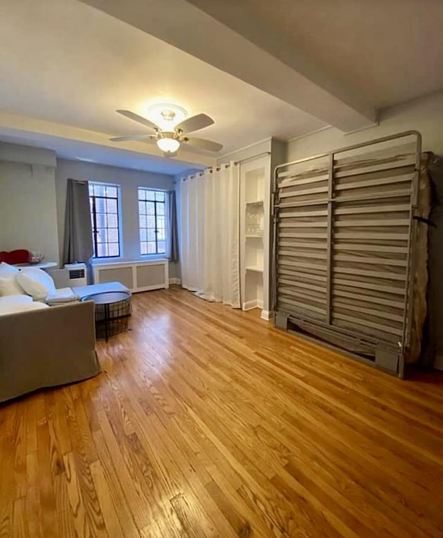 unfurnished living room with beam ceiling, radiator heating unit, wood finished floors, and a ceiling fan