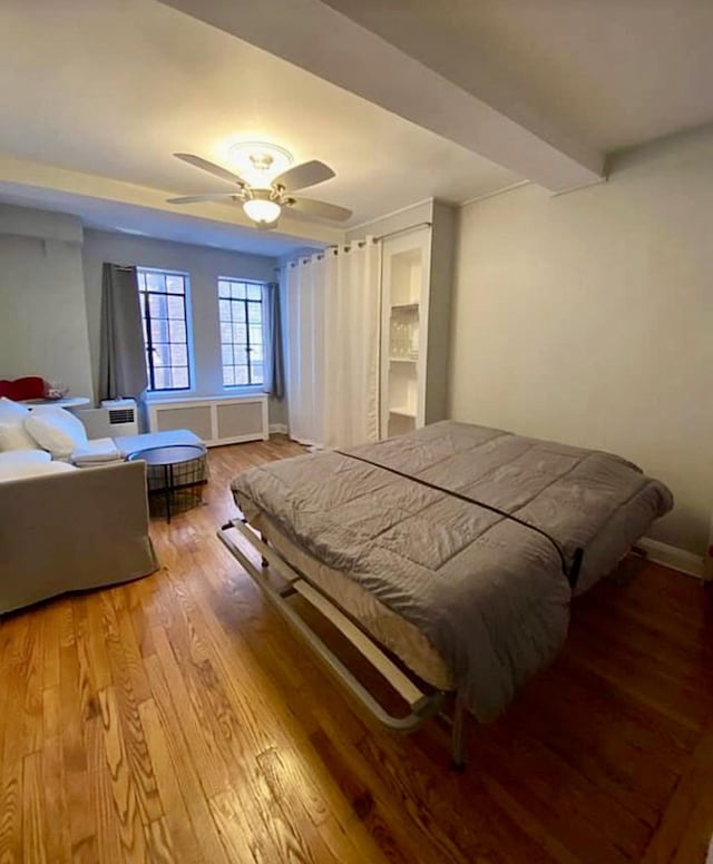 bedroom with radiator, ceiling fan, wood finished floors, beamed ceiling, and baseboards