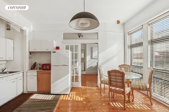 kitchen with visible vents, a sink, white cabinetry, freestanding refrigerator, and light wood-style floors