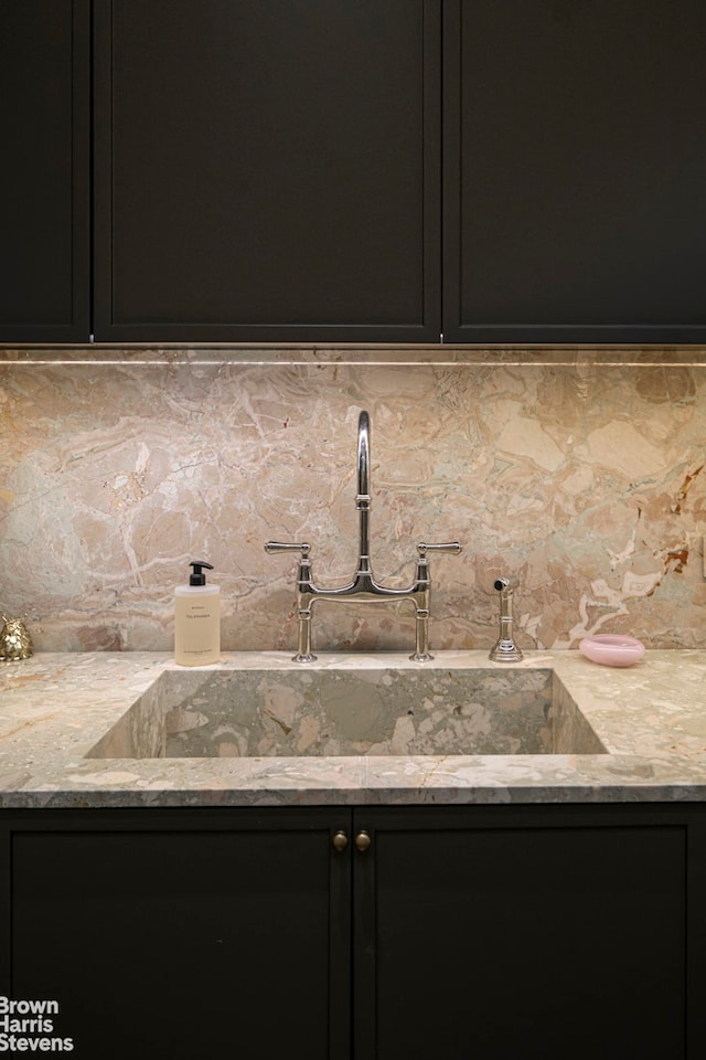 interior space featuring dark cabinets, a sink, light stone counters, and tasteful backsplash