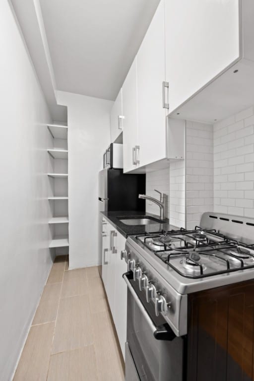 321 E 54th St Unit 2J, New York City, NY 10022 - kitchen with range with gas cooktop, a sink, white cabinets, and backsplash