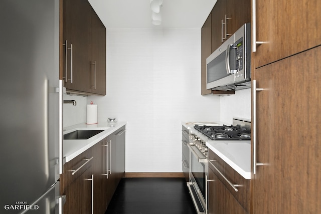 kitchen featuring dark brown cabinetry, baseboards, stainless steel appliances, light countertops, and a sink