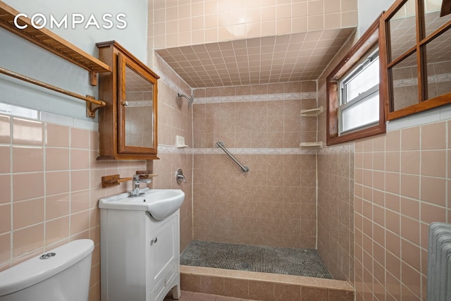 bathroom featuring vanity, radiator heating unit, a tile shower, tile walls, and toilet