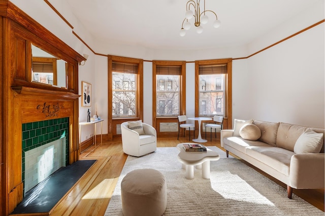 living area featuring baseboards, a tiled fireplace, light wood-style flooring, and a notable chandelier