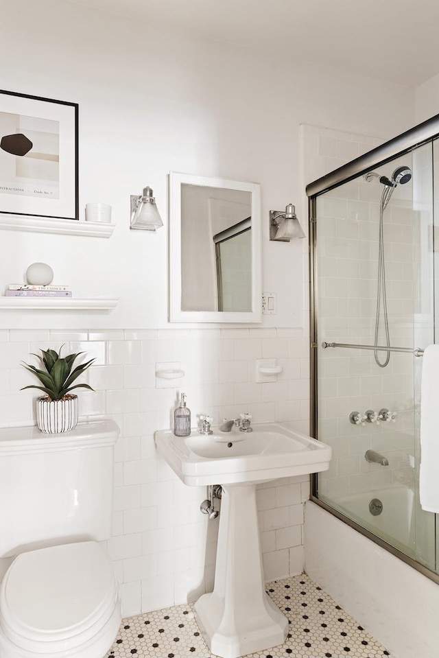 full bathroom with enclosed tub / shower combo, toilet, a wainscoted wall, and tile walls