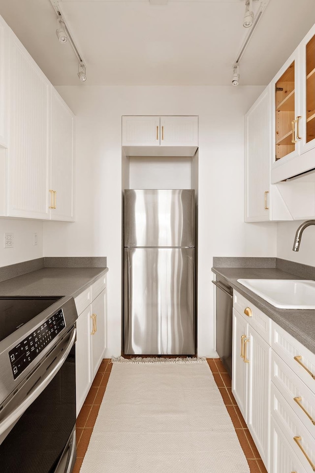 kitchen with dark tile patterned floors, a sink, white cabinets, appliances with stainless steel finishes, and glass insert cabinets