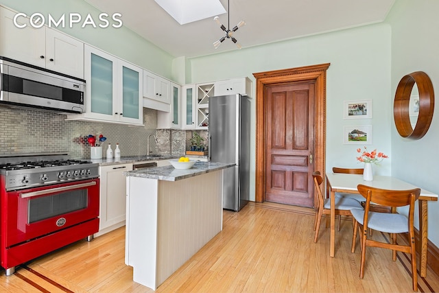 kitchen featuring a kitchen island, stainless steel appliances, light wood-style floors, a skylight, and stone counters