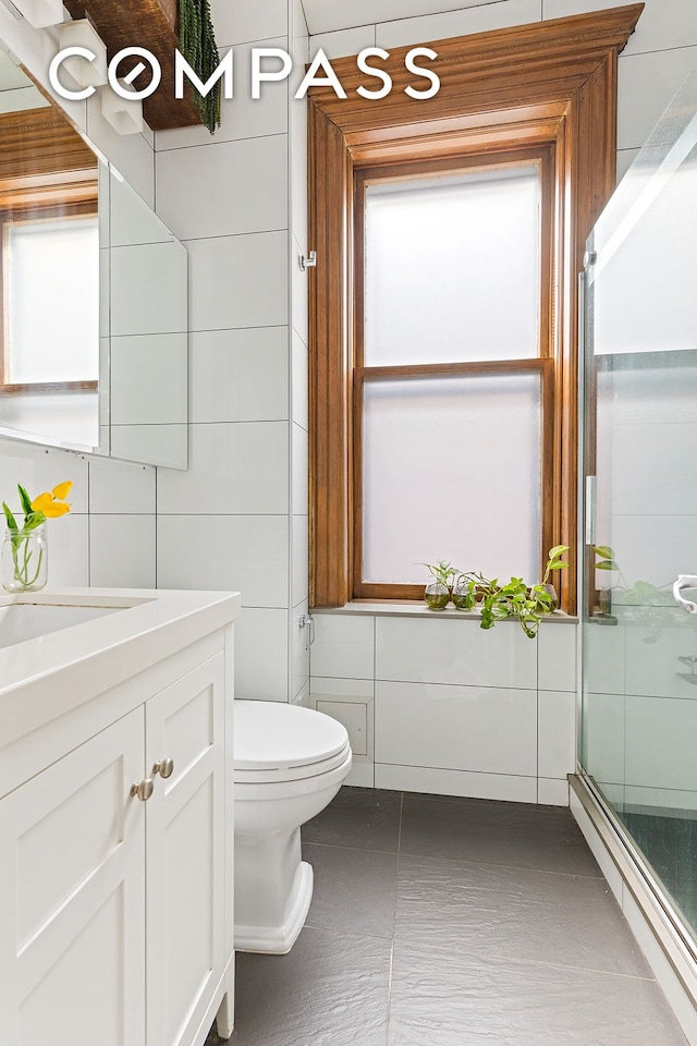 full bath featuring toilet, a stall shower, vanity, and tile walls