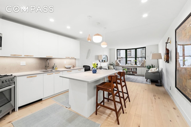 kitchen featuring a sink, light countertops, a kitchen bar, and stainless steel gas range oven