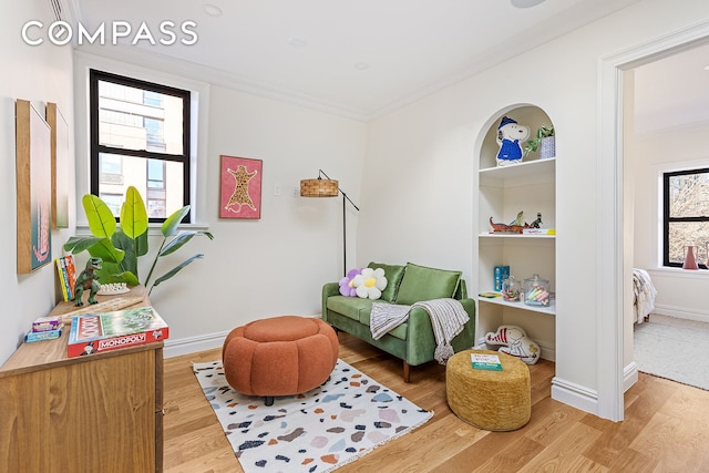 living area featuring baseboards, built in shelves, wood finished floors, and crown molding