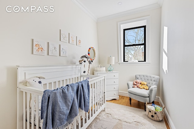 bedroom featuring crown molding, a nursery area, wood finished floors, and baseboards