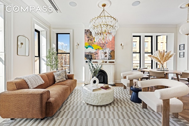 living area with wood finished floors, baseboards, a fireplace, crown molding, and a notable chandelier