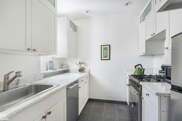 kitchen featuring light countertops, appliances with stainless steel finishes, white cabinets, a sink, and dark tile patterned floors