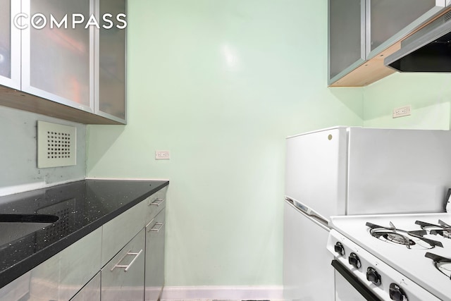 kitchen featuring dark stone countertops, glass insert cabinets, exhaust hood, and white gas stove