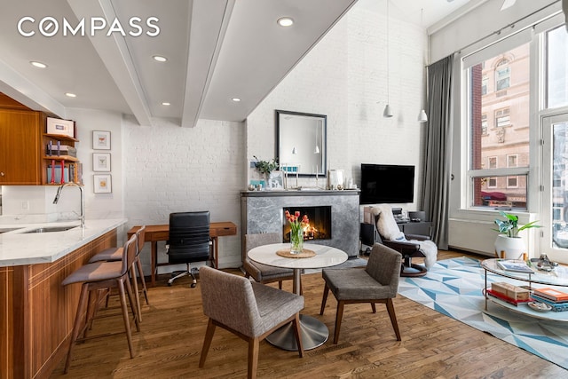 interior space with recessed lighting, brick wall, a fireplace, wood finished floors, and beamed ceiling