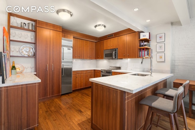 kitchen featuring a peninsula, stainless steel appliances, a sink, brown cabinets, and open shelves