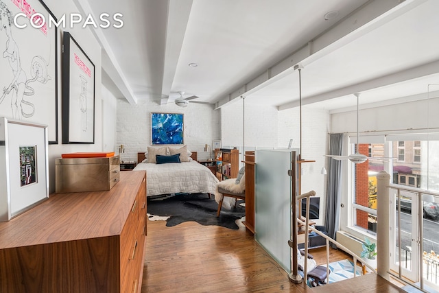 bedroom featuring brick wall, beam ceiling, and wood finished floors