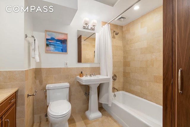 bathroom with toilet, visible vents, tile walls, wainscoting, and shower / bath combo