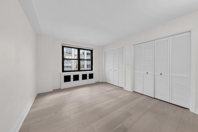 unfurnished bedroom featuring baseboards, light wood-type flooring, and multiple closets