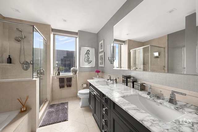 bathroom with a shower stall, tile walls, tile patterned floors, toilet, and double vanity