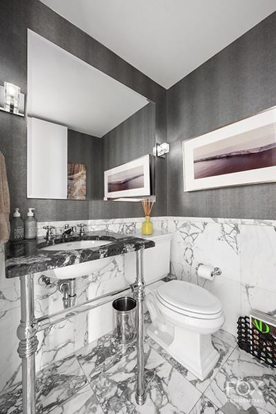 bathroom with marble look tiles, tile walls, toilet, wainscoting, and a sink