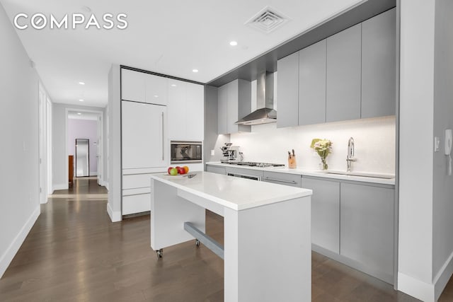 kitchen featuring visible vents, modern cabinets, built in appliances, wall chimney range hood, and a sink