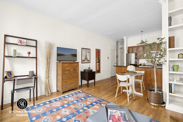 living area featuring baseboards, built in shelves, wood finished floors, and ornamental molding