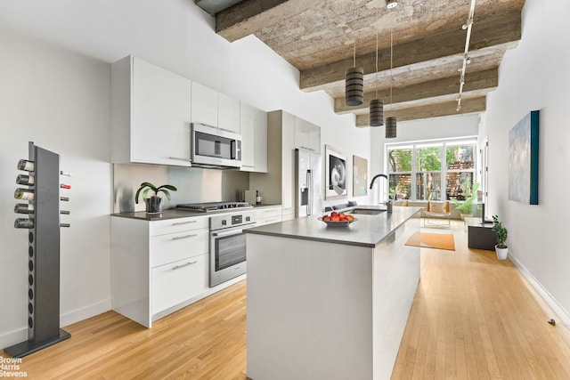 kitchen featuring light wood finished floors, dark countertops, a kitchen island with sink, stainless steel appliances, and a sink