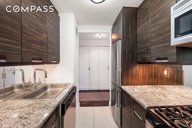 kitchen featuring tile patterned flooring, a sink, dark brown cabinetry, stainless steel appliances, and modern cabinets