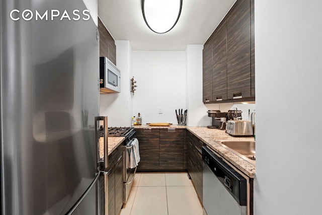 kitchen featuring dark brown cabinetry, light stone counters, light tile patterned flooring, and stainless steel appliances