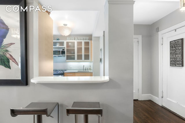 kitchen with wood finished floors, stainless steel appliances, glass insert cabinets, a kitchen bar, and backsplash