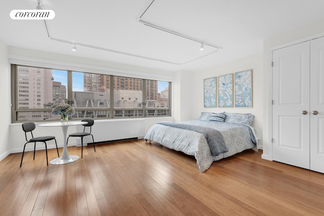 bedroom featuring baseboards, visible vents, rail lighting, wood-type flooring, and a city view