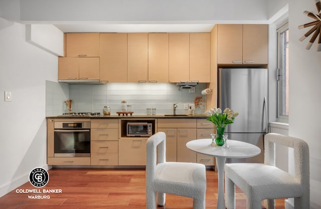 kitchen with dark countertops, backsplash, stainless steel appliances, and light wood-style flooring