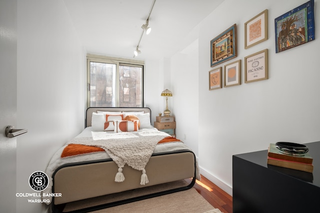 bedroom with track lighting, wood finished floors, and baseboards
