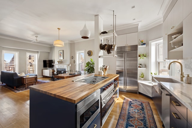 kitchen featuring white cabinets, modern cabinets, built in appliances, a fireplace, and a sink