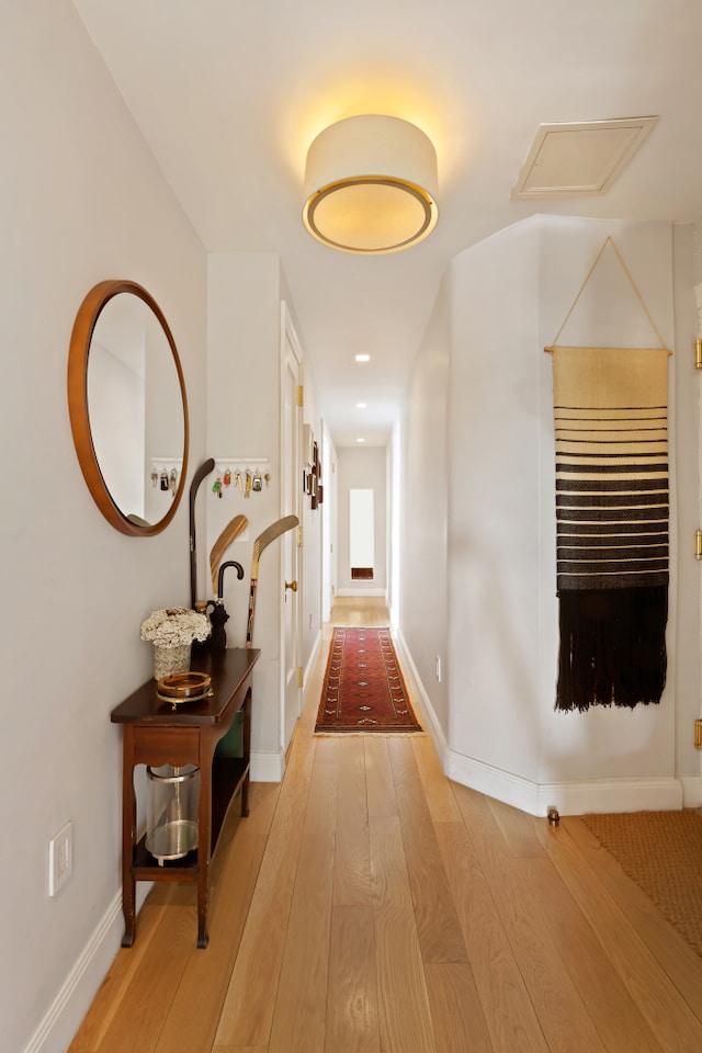 hallway featuring attic access, baseboards, and wood finished floors