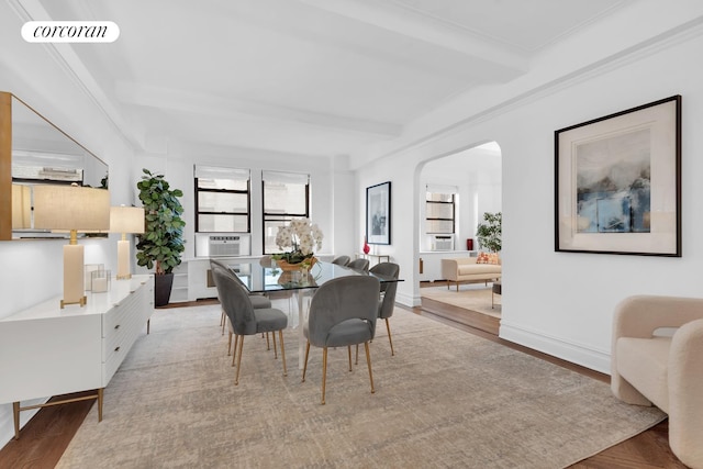 dining room featuring arched walkways, beam ceiling, light wood finished floors, visible vents, and baseboards