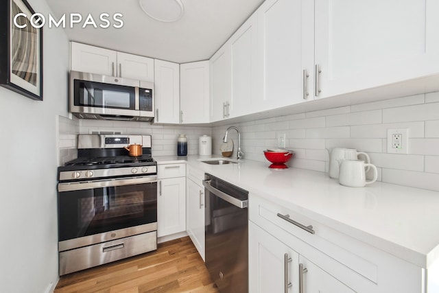 kitchen featuring tasteful backsplash, light wood-style floors, white cabinets, stainless steel appliances, and a sink