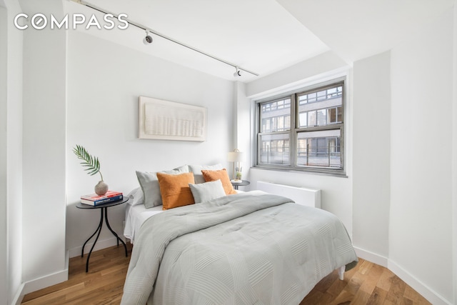 bedroom featuring rail lighting, wood finished floors, and baseboards