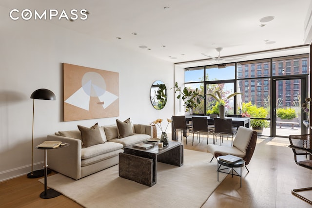 living room with baseboards, expansive windows, a ceiling fan, and wood finished floors