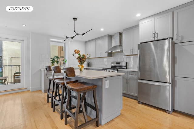 kitchen featuring visible vents, gray cabinetry, stainless steel appliances, wall chimney exhaust hood, and light wood-type flooring