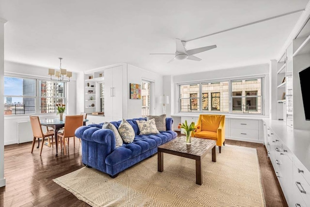 living area featuring ceiling fan with notable chandelier and dark wood-type flooring