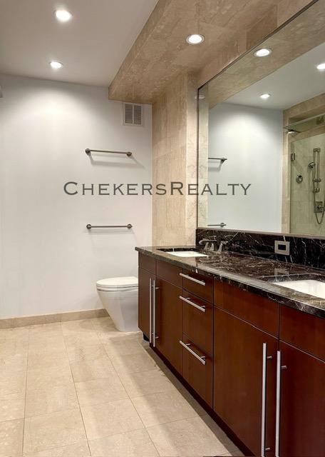 bathroom with visible vents, double vanity, a sink, a shower stall, and toilet