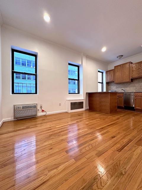 unfurnished living room featuring baseboards, light wood finished floors, crown molding, and a wall unit AC